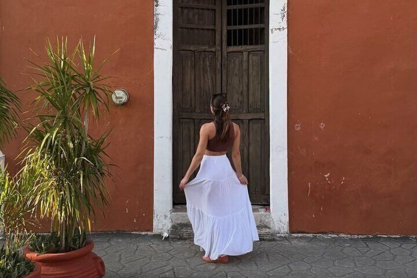 A woman in a white dress standing in front of a wooden door. 4