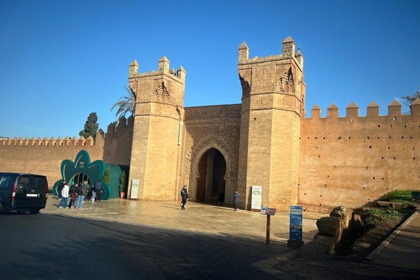 A historic stone gate with two towers, a clear sky, and a paved entrance area. 4