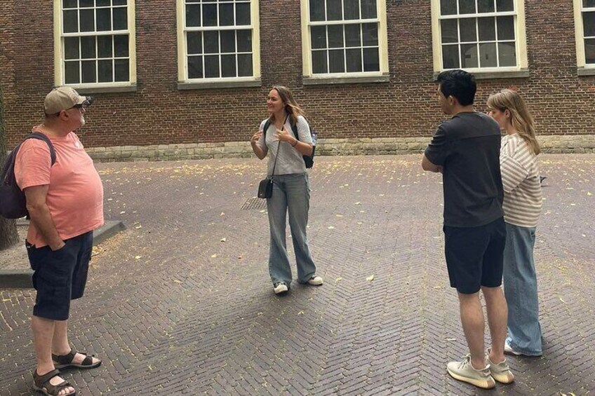 A group of people standing on a brick-paved area in front of a brick building with large windows. 1