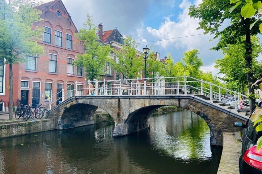 A stone bridge over a canal with red brick buildings and greenery. 4