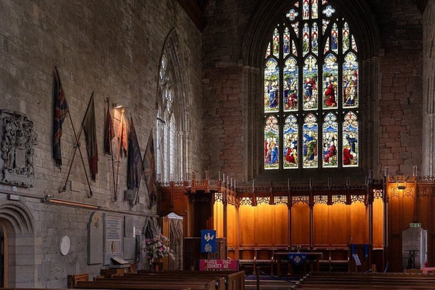 Interior de una iglesia con vidrieras, bancos de madera y banderas en la pared. 5