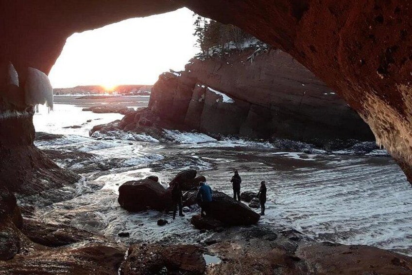 A cave entrance with people exploring the interior and a sunset in the background. 1