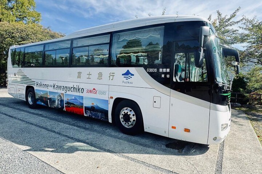 A white bus with 'Sunrise Tours' and 'Hakone' branding, parked on a road with trees in the background. 2