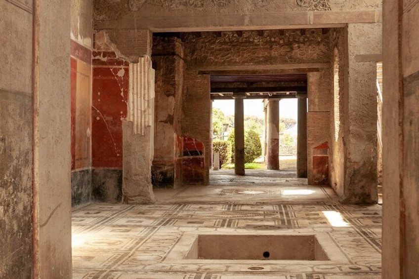An ancient Roman bath with stone columns, a central pool, and intricate floor mosaics. 2