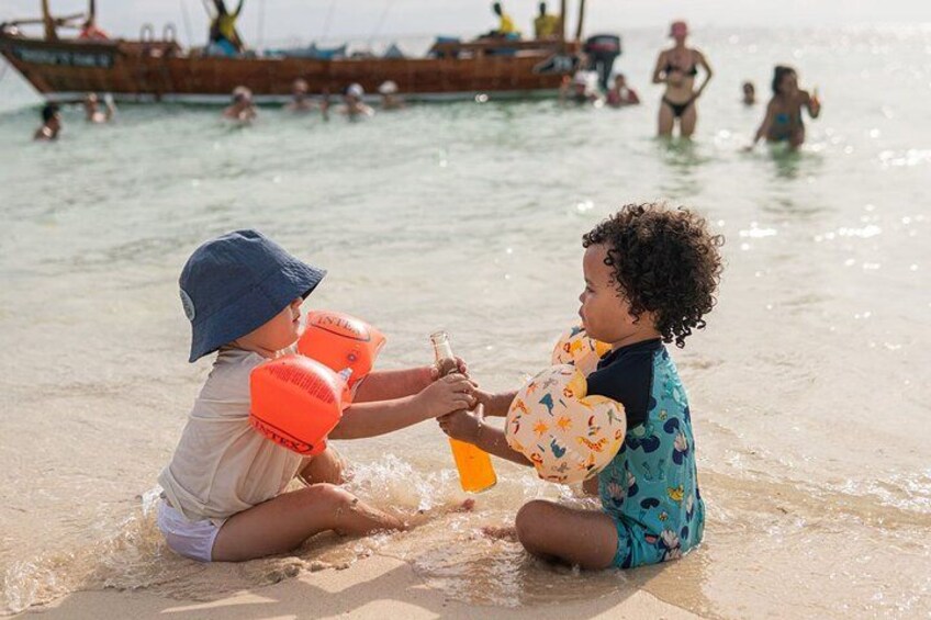 Two children playing with sand toys on a beach with boats in the background. 3