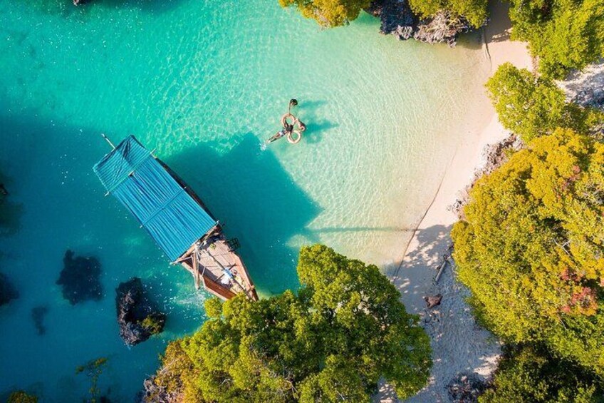 A clear turquoise sea, a small boat docked on a sandy beach, and dense green foliage. 4