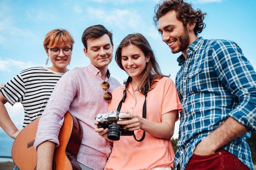 A group of people standing outdoors, one holding a guitar, another with a camera, and a third holding a drink. 1