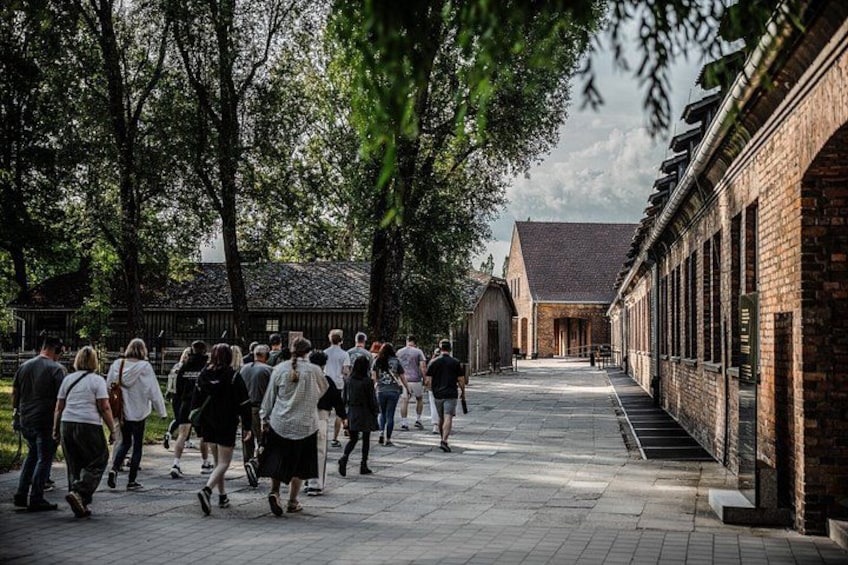 A group of people walking on a paved path in a park-like setting with trees and brick buildings. 2