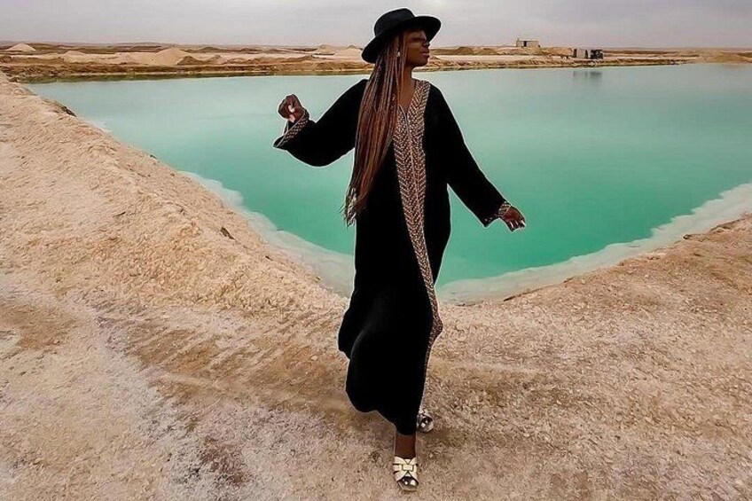 A person standing by a turquoise body of water with a desert landscape in the background. 2