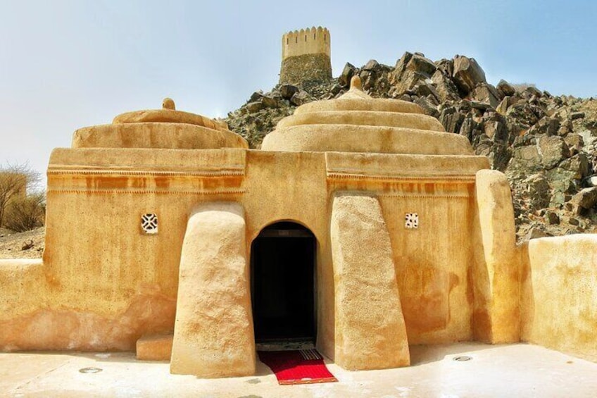 A historical building with a central archway and two domes, set against a rocky landscape. 1