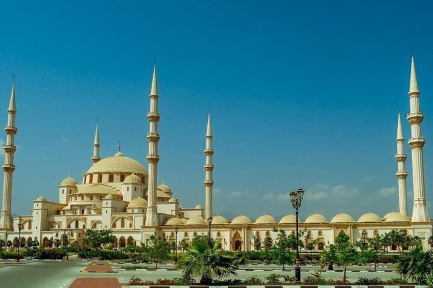 A mosque with multiple minarets and domes, surrounded by a landscaped area with palm trees and a clear sky. 5