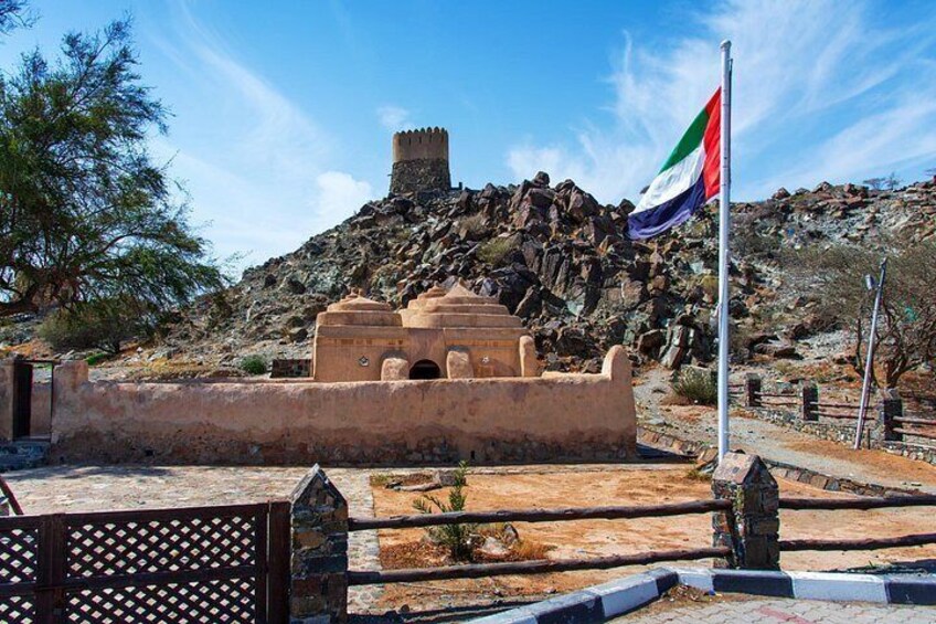 A historical fortification, a flagpole with the UAE flag, and a rocky landscape. 3
