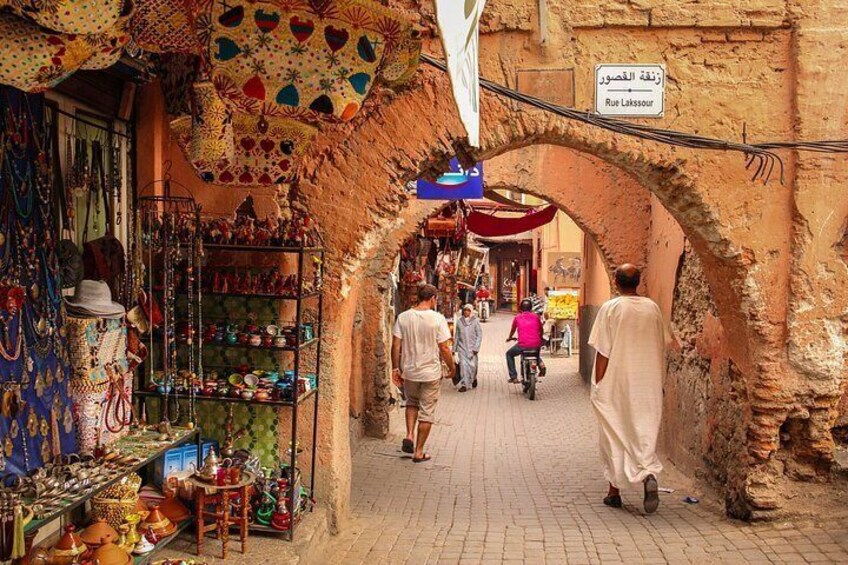 A narrow street with shops on either side, an archway, and a sign indicating Rue Lakesour. 1