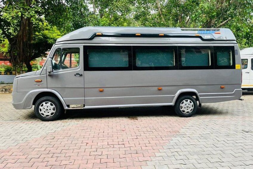 Un autobus grigio parcheggiato su un marciapiede in mattoni, con alberi sullo sfondo. 1