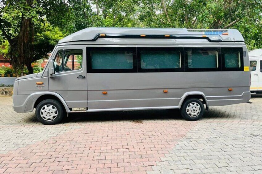 A gray bus parked on a brick pavement with trees in the background. 1