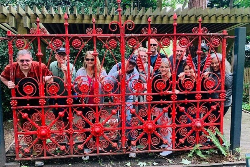 A group of people posing behind a red metal gate with intricate designs. 3