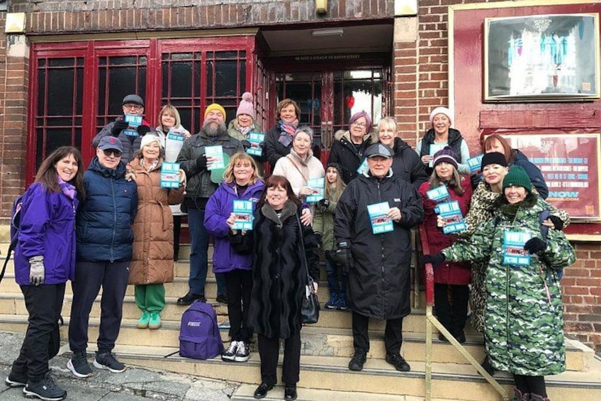 A group of people standing outside a building with red doors, holding books. 2
