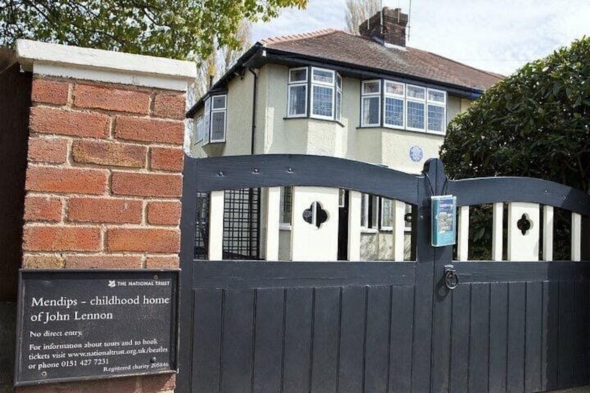 A gated entrance to a house with a sign indicating it's the childhood home of John Lennon. 4