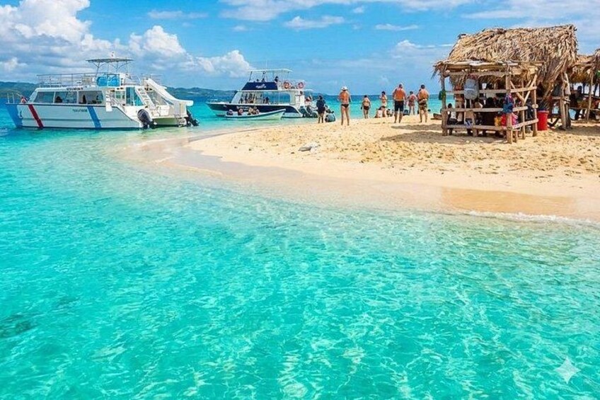 A beach with clear turquoise water, boats, and people. 2