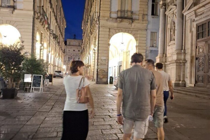 A nighttime street scene with people walking, historic buildings, and illuminated signs. 5