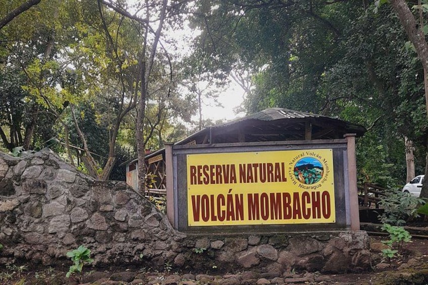 Naamplaatje voor Reserva Natural Volcán Nombacho, met een stenen muur en bomen op de achtergrond. 5