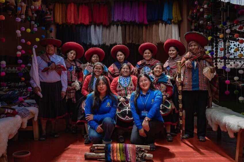 Un groupe de personnes, vêtues de costumes traditionnels aux tissus colorés et coiffées de chapeaux rouges, posent dans un décor intérieur aménagé. 1