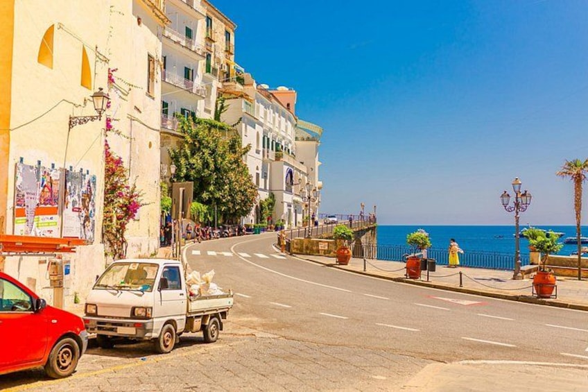 A coastal street with parked vehicles, buildings, and a clear blue sky. 2