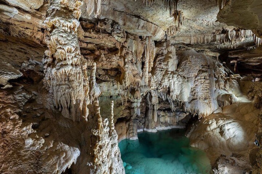 A cave with stalactites, stalagmites, and a pool of water. 4