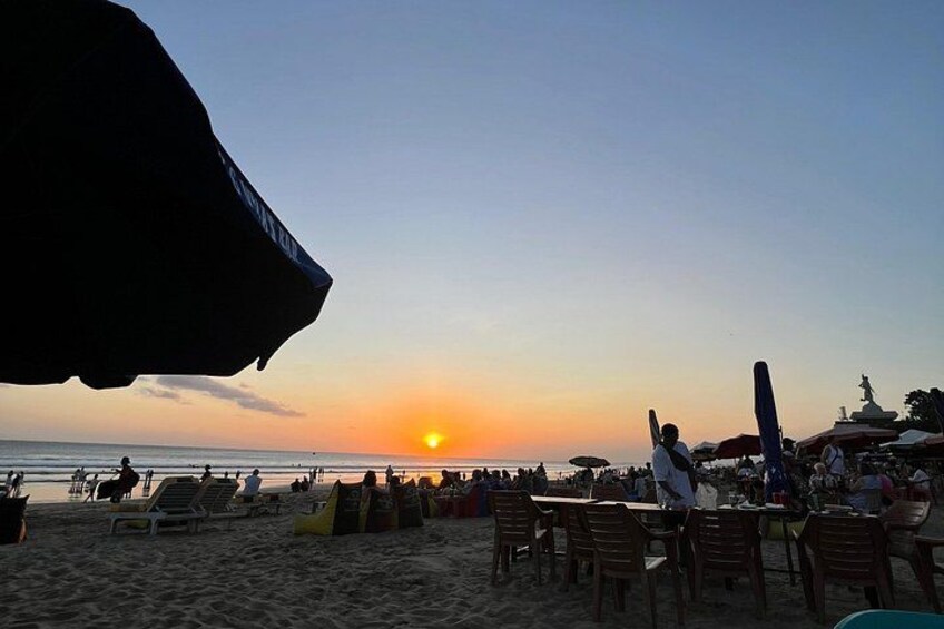 En strand ved solnedgang med mennesker, stole og parasoller. 5