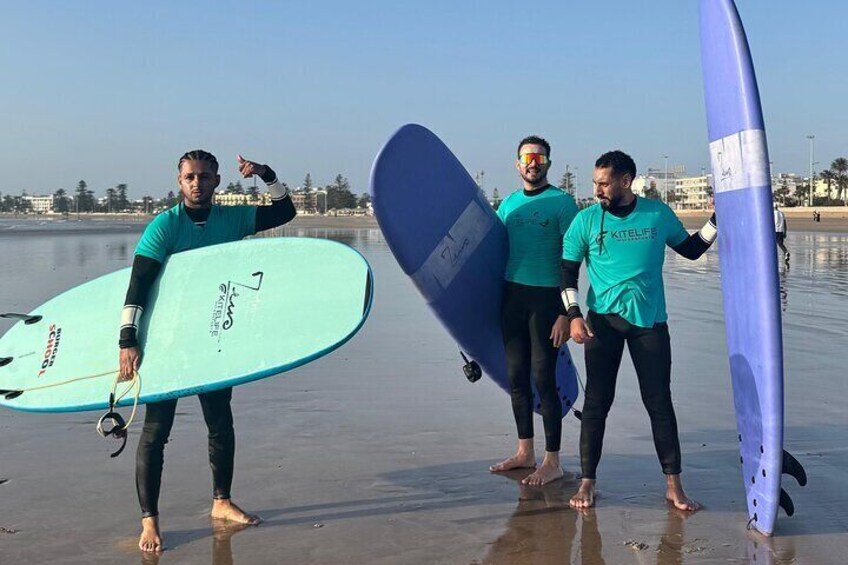 Trois personnes tenant des planches de surf sur une plage. 3