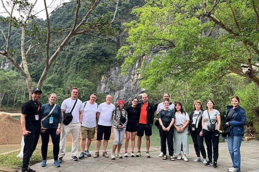A group of people standing outdoors with trees and a rocky cliff in the background. 5