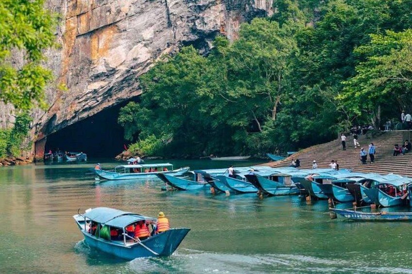 A river with boats docked near a cave entrance, surrounded by lush greenery. 1