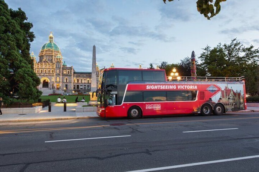 A red sightseeing bus with 'SIGHTSEEING VICTORIA' written on the side, parked on a street with a large building in the background. 2