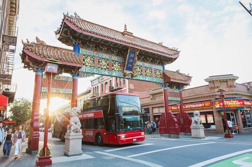 A red double-decker bus at a traditional Chinese gate with a restaurant in the background. 3