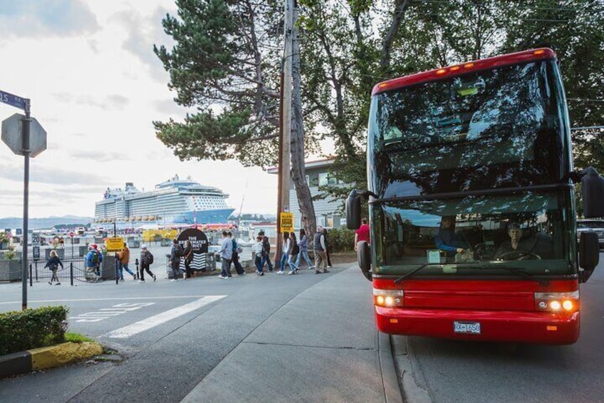A red double-decker bus on a city street with people walking and a cruise ship in the background. 1