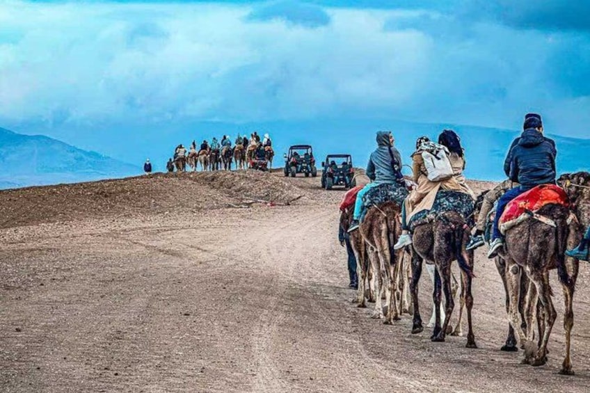 Un groupe de personnes chevauche des chameaux sur un chemin de terre, avec un paysage montagneux en arrière-plan. 4