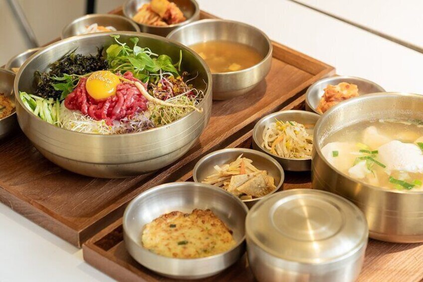 A variety of Korean dishes including a bowl of raw beef topped with an egg, side dishes, and a bowl of soup. 4
