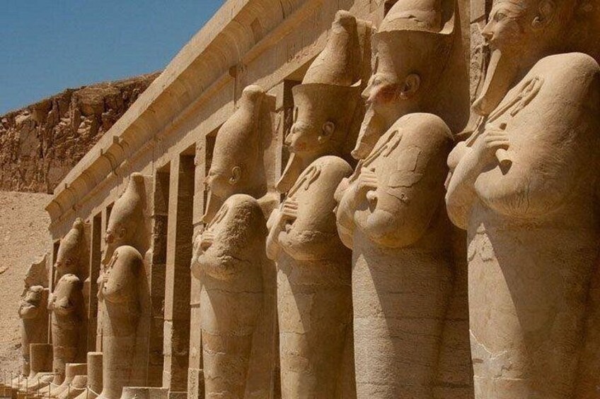 A row of ancient Egyptian statues with outstretched arms, set against a desert backdrop. 2