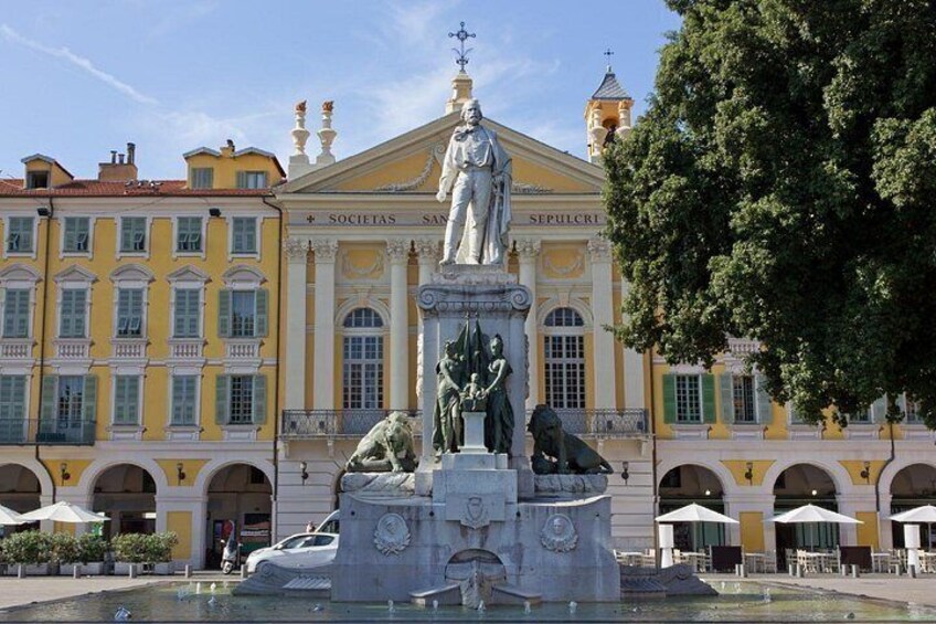 Une statue se trouve devant un bâtiment jaune, doté de fenêtres en arc de cercle et d’une fontaine ornée de lions. 2