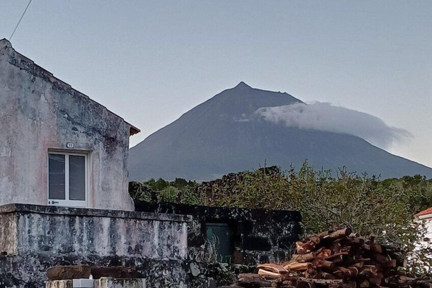 A house with a window, a mountain with smoke, and some vegetation in the foreground. 4
