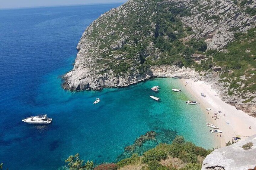 Un paysage côtier caractérisé par une eau turquoise cristalline, une plage de sable, des falaises rocheuses et plusieurs bateaux ancrés près du rivage. 2