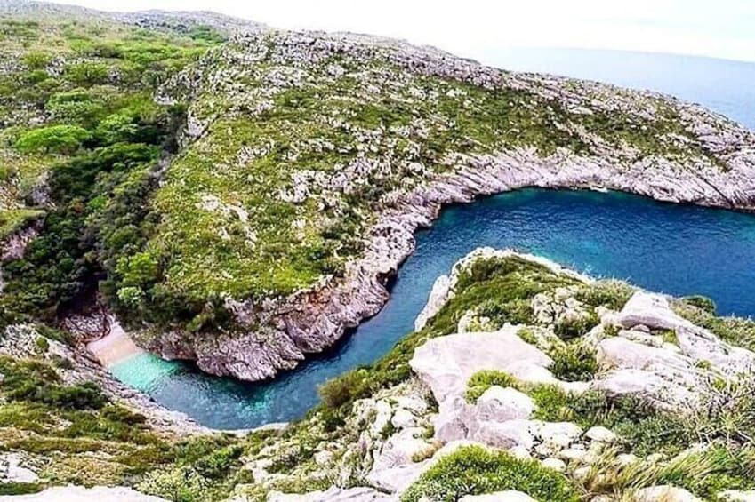 A coastal landscape with rocky cliffs, a narrow waterway, and lush greenery. 1