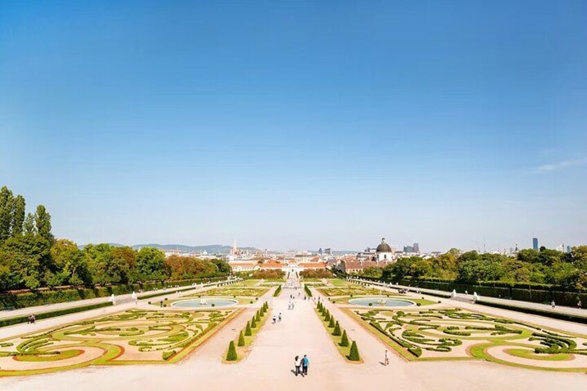 Un jardín grande y simétrico con césped cuidado, diseños geométricos y un camino central que conduce a un edificio con cúpula. 3