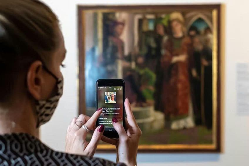 En person holder en smartphone med en galleri-app åben, foran et indrammet maleri. 4