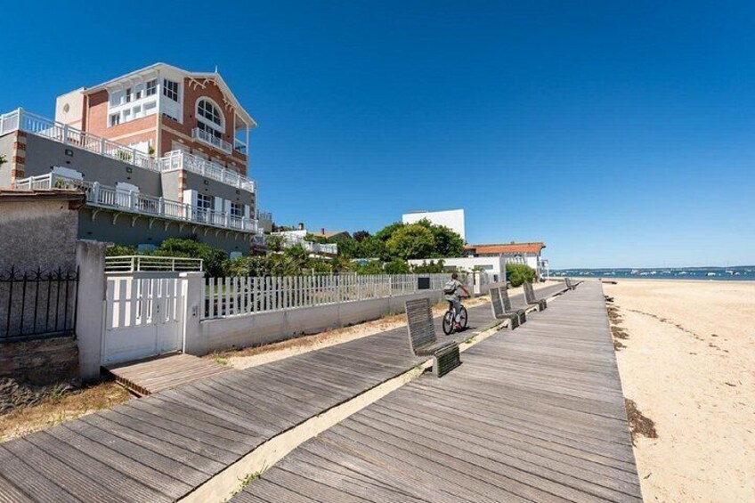 Un muelle de madera bordeando una playa, una casa grande con balcón y un cielo azul despejado. 4