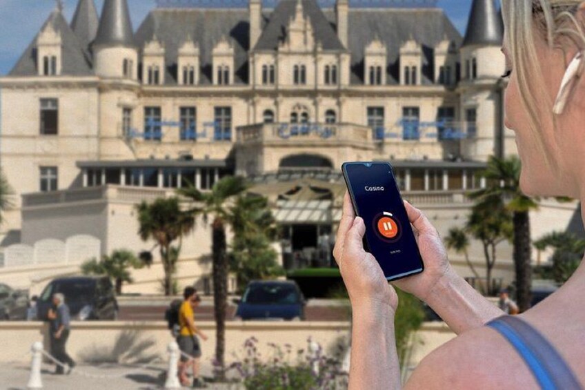 A person holding a smartphone with a casino app, in front of a large, ornate building with multiple towers and a balcony. 2