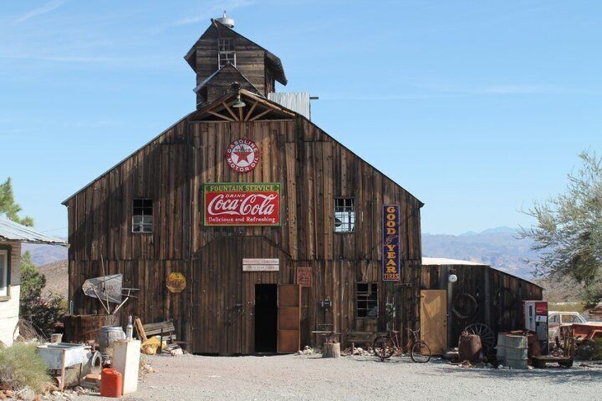 A wooden building with a Coca-Cola sign, a fountain service sign, and a 'Good Year' sign. 4