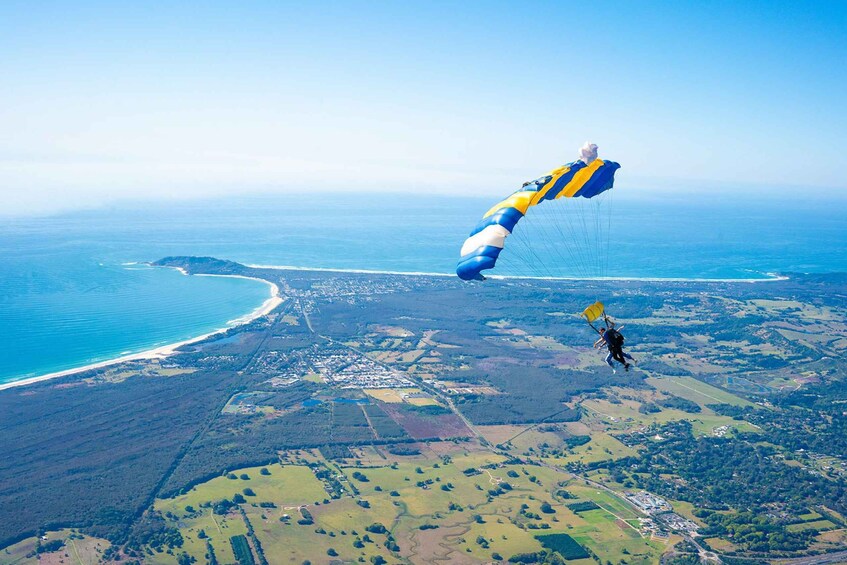 A person skydiving with a parachute over a coastal landscape. 2