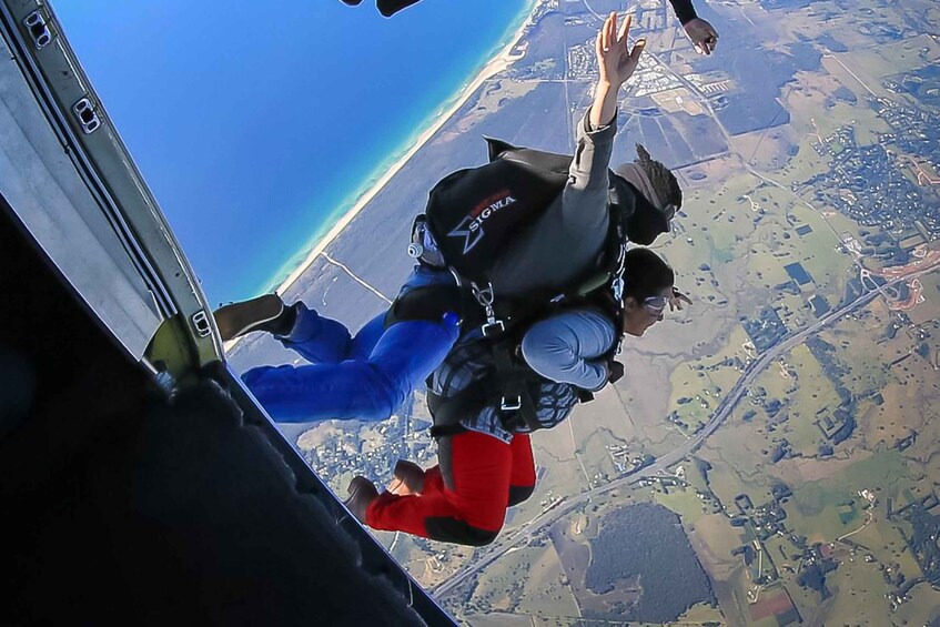 Two skydivers in freefall with a beach and farmland below. 4