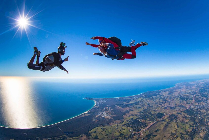 Two skydivers in freefall with a coastal landscape below. 1